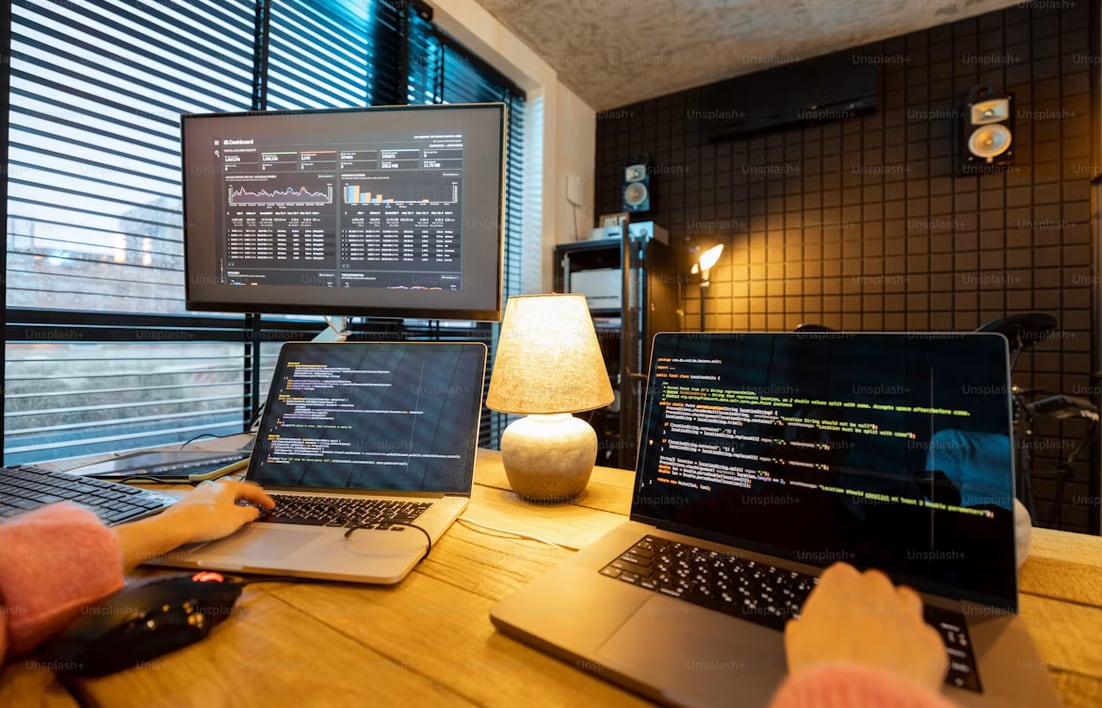A desk mid-session: laptops, a dashboard on the monitor, hands on the keyboard